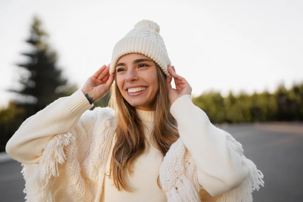happy-woman-in-cold-weather smiling young blond woman walking in winter park having fun wearing warm white knitted sweater